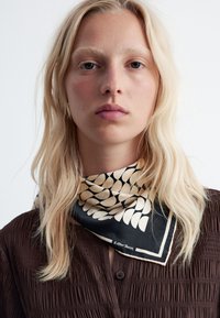 Seidenschal mit schwarzem Hintergrund, cremefarbenen abstrakten Mustern und einem kontrastierenden Rand. Glatte Textur, leichtes Design.