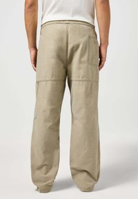 Beżowe spodnie cargo o luźnym kroju, z elastycznym pasem, bocznymi kieszeniami i widocznymi szwami; miękka faktura materiału.