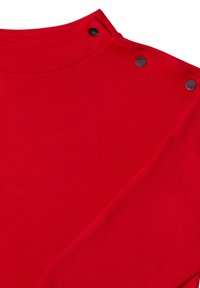 Haut rouge à manches longues en tissu lisse. Présente un col montant avec trois boutons pression noirs sur l'épaule, soulignant la simplicité du design.