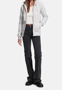 Sudadera con capucha gris claro con cremallera y cordón, combinada con vaqueros negros acampanados de talle alto y botas negras con suela gruesa.