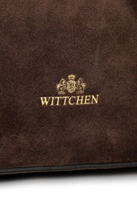 Borsa in suede marrone con una texture liscia, dotata di un logo dorato "WITTCHEN" e uno stemma decorativo. Design semplice ed elegante.
