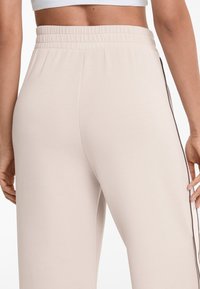 Helle beige, locker sitzende Hosen mit einem elastischen Bund und kontrastierenden braunen Seitenstreifen. Weiche Textur, entworfen für Komfort und Bewegungsfreiheit.