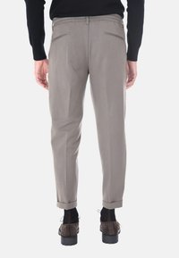 Pantaloni grigi a tapered con vestibilità comoda e vita elasticizzata. Presentano due tasche posteriori e polsi arrotolati. Indossati con scarpe marroni.