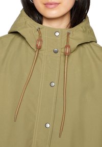 Płaszcz przeciwdeszczowy oliwkowozielony z kapturem, zapinany na zatrzaski, z regulowanymi ściągaczami i kontrastowymi przeszyciami.