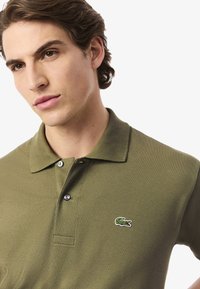 Oliwkowa koszulka polo wykonana z teksturowanej bawełny, z dwoma guzikami na plastrze oraz małym haftowanym logo krokodyla na lewej piersi.