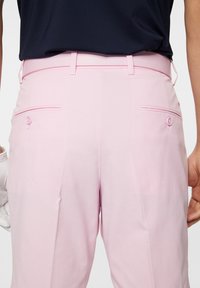 Vaaleanpunaiset golf-housut, joissa on teksturoitu pinta, kaksi takataskua, nappikoristeet ja sileä, muotoiltu vyötärö.