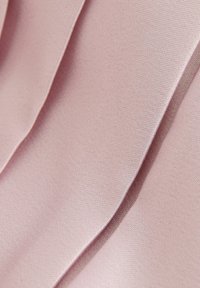 Tessuto rosa chiaro con pieghe verticali. Texture liscia con una leggera lucentezza e un design strutturato.