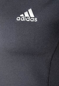 Black sports shirt made of stretchy fabric featuring an Adidas logo in white. The design is sleek with visible seams and a smooth texture.