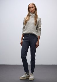 Jasnoszary sweter z golfem o teksturowanym wzorze, zestawiony z granatowymi spodniami typu slim fit z bocznymi kieszeniami i zapięciem na guzik.
