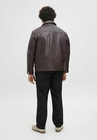 Brown leather jacket with a high collar, visible stitching details, and silver hardware. Paired with black pants and light-colored shoes.