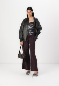 Black leather bomber jacket, floral print top, striped maroon wide-leg pants, silver heeled shoes, and a small brown purse.