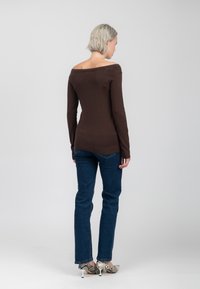 Brauner, langärmeliger Sweater mit Off-Shoulder-Design, kombiniert mit dunkelblauen Jeans und gemusterten High Heels.