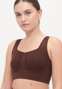 Brown sports bra with a square neck, wide straps, and textured center seam. Smooth fabric with a fitted design. Simple, clean lines.