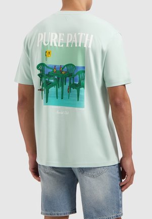 Mintgroene t-shirt met korte mouwen, met een kleurrafische afbeelding van groene stoelen en tafels, met daarboven de tekst "PURE PATH". Zacht katoenmateriaal.