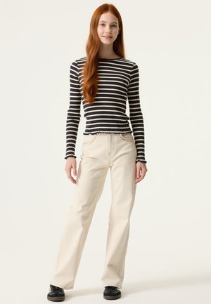 Zwart-wit gestreepte, geribbelde top met lange mouwen en een geschulpte zoom, gecombineerd met lichtbeige wijde broekspijpen en zwarte sneakers.
