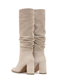Beżowe zamszowe botki do kolan z marszczonym wzorem, kwadratowym czubkiem i masywnym obcasem. Posiadają złoty zamek z boku, co ułatwia zakładanie.