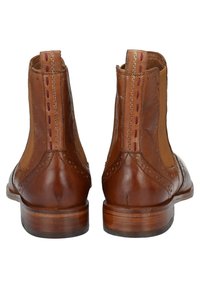 Bottines en cuir marron avec panneaux latéraux en élastique, détails de brogue et un talon empilé. Présente des coutures contrastantes en marron.