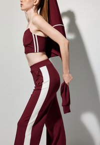 Bordeaux sportieve set met een strapless crop top met witte zijkanten en bijpassende high-waisted broek met pockets en zijkantaccenten.