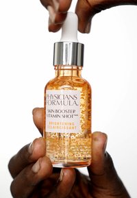 Liquido ambrato in una bottiglia a goccia trasparente, con un tappo argentato e un contagocce bianco. Piccole perle dorate visibili all'interno. 30 mL.