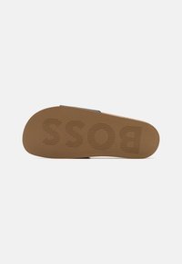 Semelle de sandale en caoutchouc marron avec le nom de marque "BOSS" en relief, présentant un motif texturé pour une meilleure adhérence et des bords lisses.
