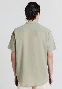 Kurzärmliges Hemd aus mattgrünem, strukturiertem Stoff mit lockerer Passform und Button-Down-Kragen. Hat einen schlichten Rücken und einen geraden Saum.