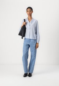 Camicia blu chiaro a righe con colletto a volants, abbinata a jeans blu chiaro a fantasia e stivaletti neri alla caviglia; borsa a tracolla nera in mano.