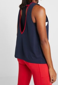 Marinblå linne med röda detaljer, har en utskuren ryggdesign, tillverkat i lättviktsmaterial. Kombineras med röda stretchiga leggings.