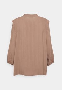 Blusa a maniche lunghe color marrone chiaro, caratterizzata da un motivo testurizzato, vestibilità morbida e polsini arricciati. Colletto e schiena semplici.