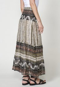 Lange, gestreepte rok met een elastische zwarte tailleband. Heeft geometrische ontwerpen in beige, bruin en zwart. Lichtgewicht stof met een vloeiende silhouet.