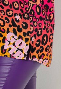 Bright leopard-print fabric in orange and pink with "GOVT" text over purple shiny leggings.