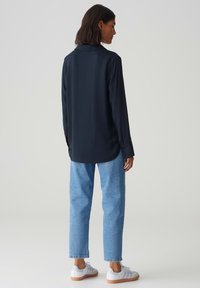 Camicia a maniche lunghe blu navy con colletto, vestibilità comoda, abbinata a jeans dritti azzurri e sneakers bianche. Tessuto dalla texture liscia.