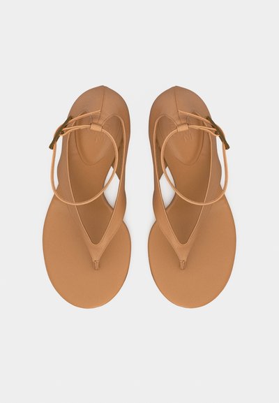 Ταν δερμάτινα σανδάλια με επίπεδη σόλα, λουριά αστραγάλου και θηλιές δακτύλων, από πάνω σε λευκό φόντο.