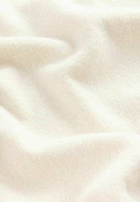 Weicher Creme-Stoff mit glatter Textur, der sanfte Falten und subtile Farbvariationen zeigt, was auf ein leichtes Material hinweist.
