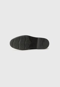 Talpa de pantof din cauciuc negru, cu o suprafață texturată, având un model ondulat și puncte circulare de prindere pentru tracțiune. Finisaj neted pe margine.