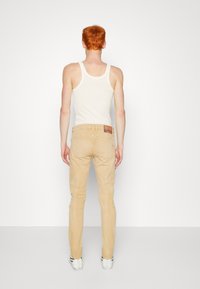 Chinos de corte slim en un color claro, con pasadores para cinturón y un bolsillo parche en la parte trasera. La tela parece suave con una textura sutil.