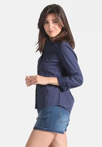 Chemise bleu marine à boutonnière avec un col et des manches retroussées, associée à un short en denim avec des poches arrière et un ourlet effiloché.