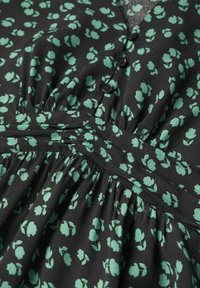 Robe noire avec petit imprimé floral vert, boutons sur le devant et tissu froncé à la taille et à la poitrine.