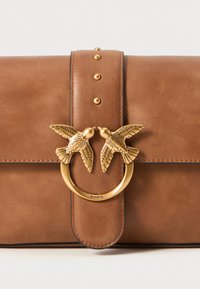 Bruine leren clutch met een decoratieve goudkleurige sluiting met twee vogelmotieven en studs langs de klep.