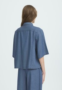 Kurze Ärmel Jeanshemd in Mittelblau mit lockerer Passform, Button-Down-Kragen und einer einzelnen Rückennaht. Texturiert.