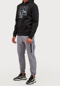 Svart hooded sweatshirt med framgrafik, parat med ljusgrå tapered byxor med blixtlåsfickor, bärs med svarta och grå sneakers.
