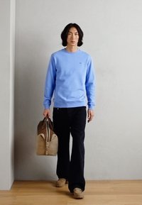 Felpa azzurra, jeans neri, borsa beige e zoccoli color tan. La felpa ha un collo rotondo; la borsa ha un design bicolore.