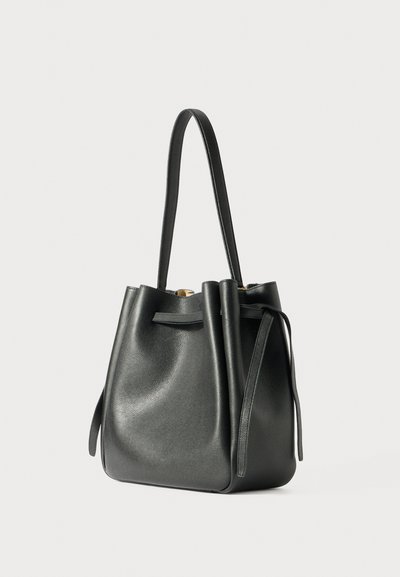 Fekete bőr vödör táska két felső fogantyúval, puha textúrával, kerek formával és díszes oldalszíjakkal. Arany tónusú fém részletekkel rendelkezik.