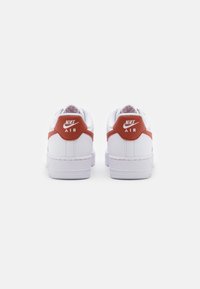 Fehér Nike Air sportcipő, piros részletekkel a saroknál és az oldalsó logón, sima bőr anyagból készült, klasszikus alacsony fazon.