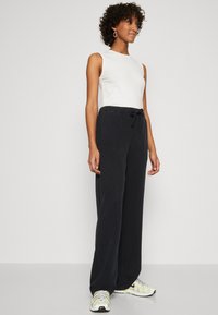 Black wide-leg pants with a drawstring waist, paired with a fitted white sleeveless top and multicolored athletic shoes. Smooth texture.