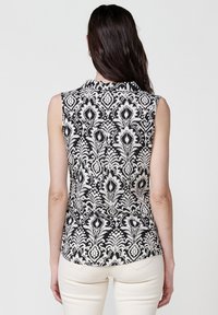 Canottiera senza maniche con motivo floreale in bianco e nero, realizzata in tessuto leggero con colletto e orlo curvo. Presenta una vestibilità dritta.