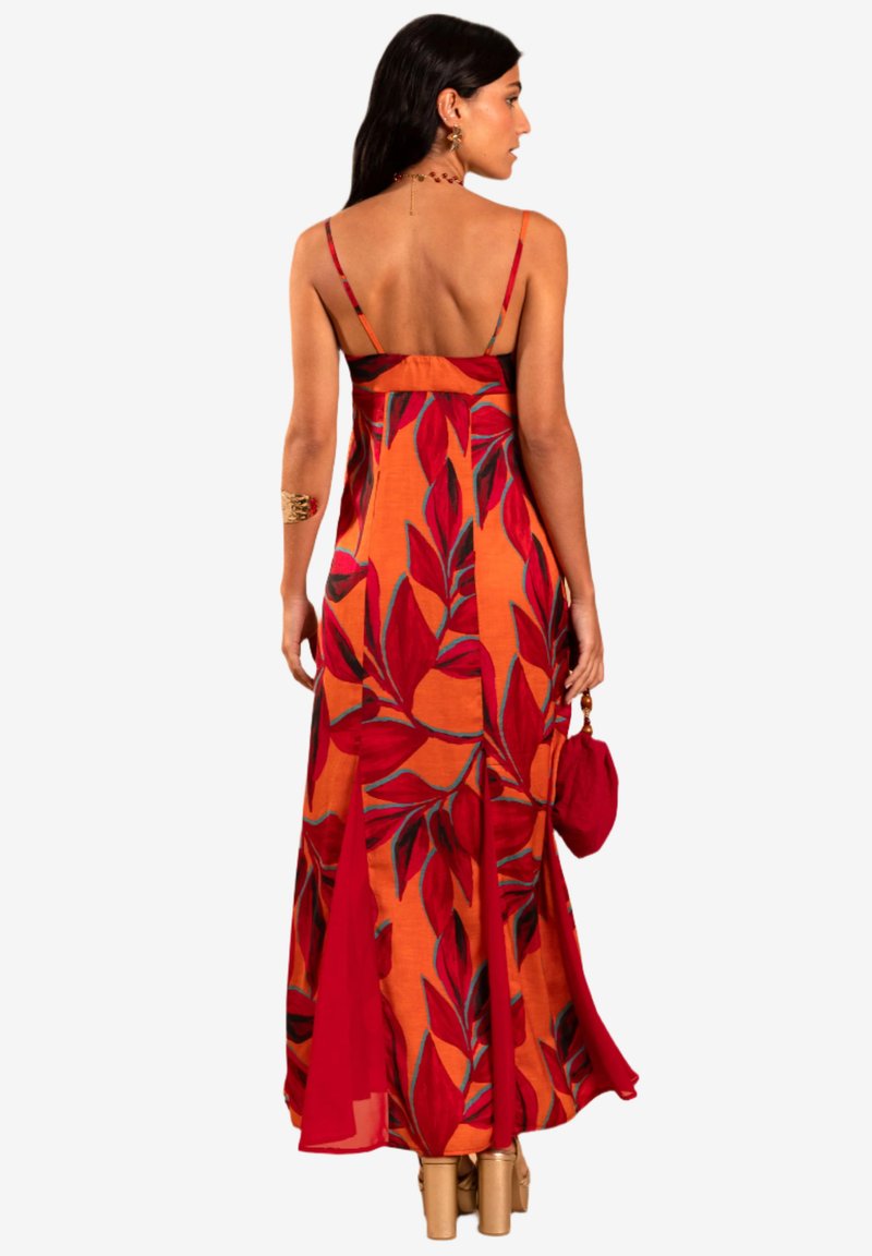 Robe longue sans manches mettant en avant un tissu orange vif avec des imprimés de feuilles rouges et vertes. Des accents transparents et un design fluide améliorent sa silhouette.