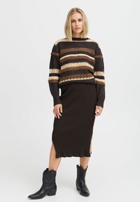 Gestreifter Strickpullover in Braun und Creme, kombiniert mit einem gerippten braunen Rock mit seitlichen Schlitzen, getragen mit schwarzen Cowboystiefeln.