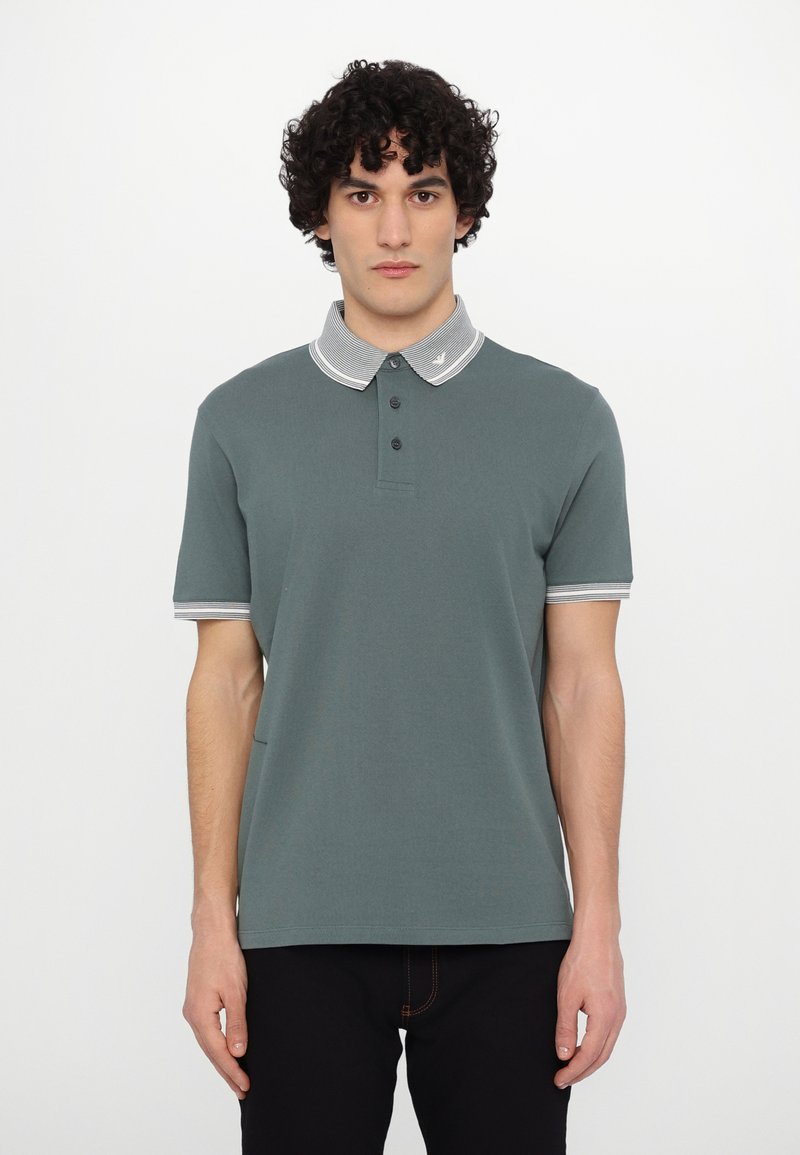 Grønn polo med stripete grå krage, tre-knapps placket, korte ermer og slim fit. Materialet har en myk tekstur.