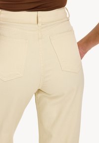 Jeans de tiro alto en color beige con una silueta ajustada, que presentan dos bolsillos traseros con costuras sutiles y una textura de denim suave.