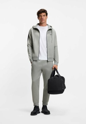 Grå sweatshirt og joggers med lynlås foran, hætte og kontrasterende sidelænestreger, parret med en sort sportstaske. Teksureret stof.
